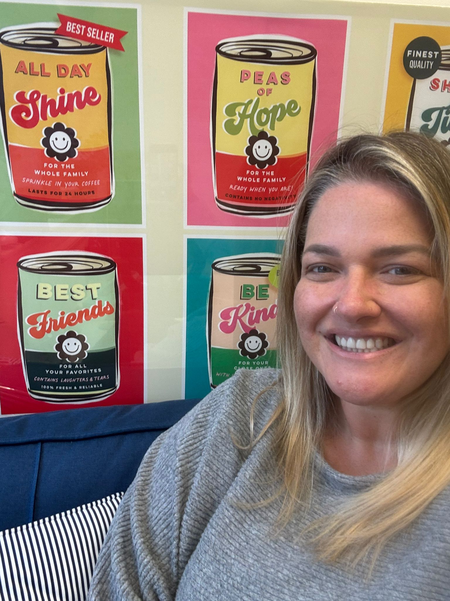 Laura King - Youth Coach sitting against a wall with pop-art style quotes of positive affirmations in the style of cans of soup.